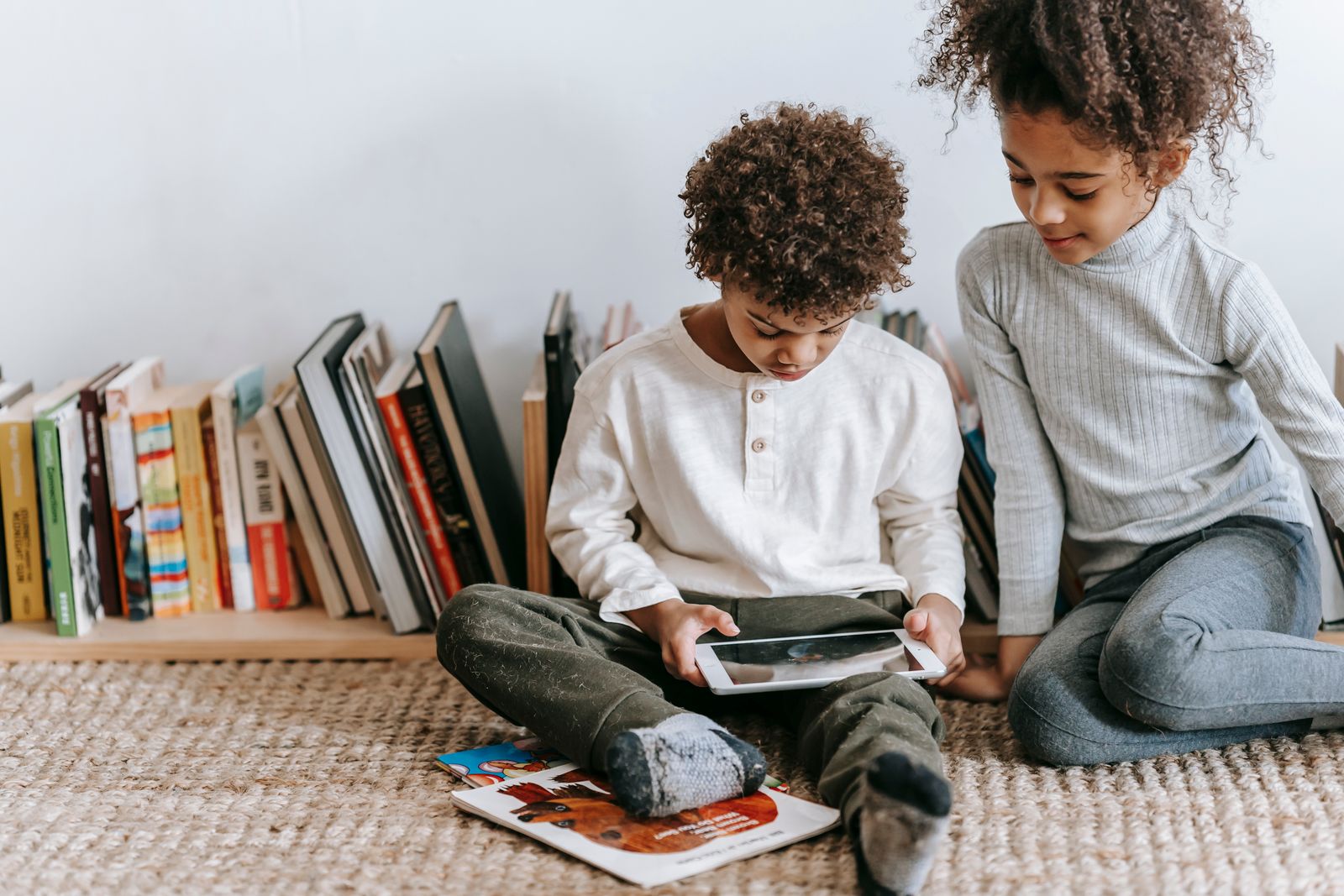 Two children reading a story together on a tablet beside a shelf of books